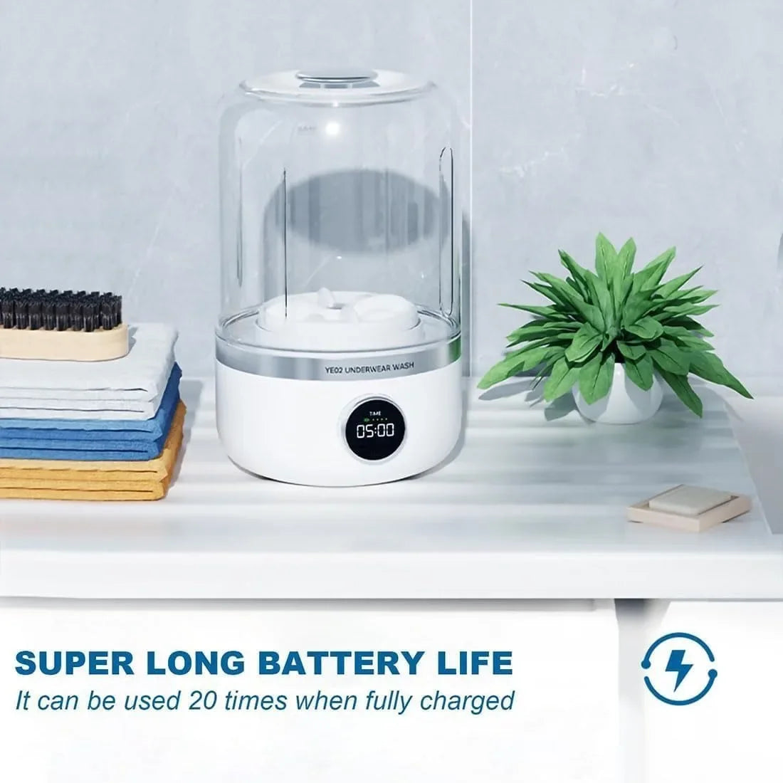 White electronic EDGAB mini washing machine with digital display on a white surface with a plant and books in the background.