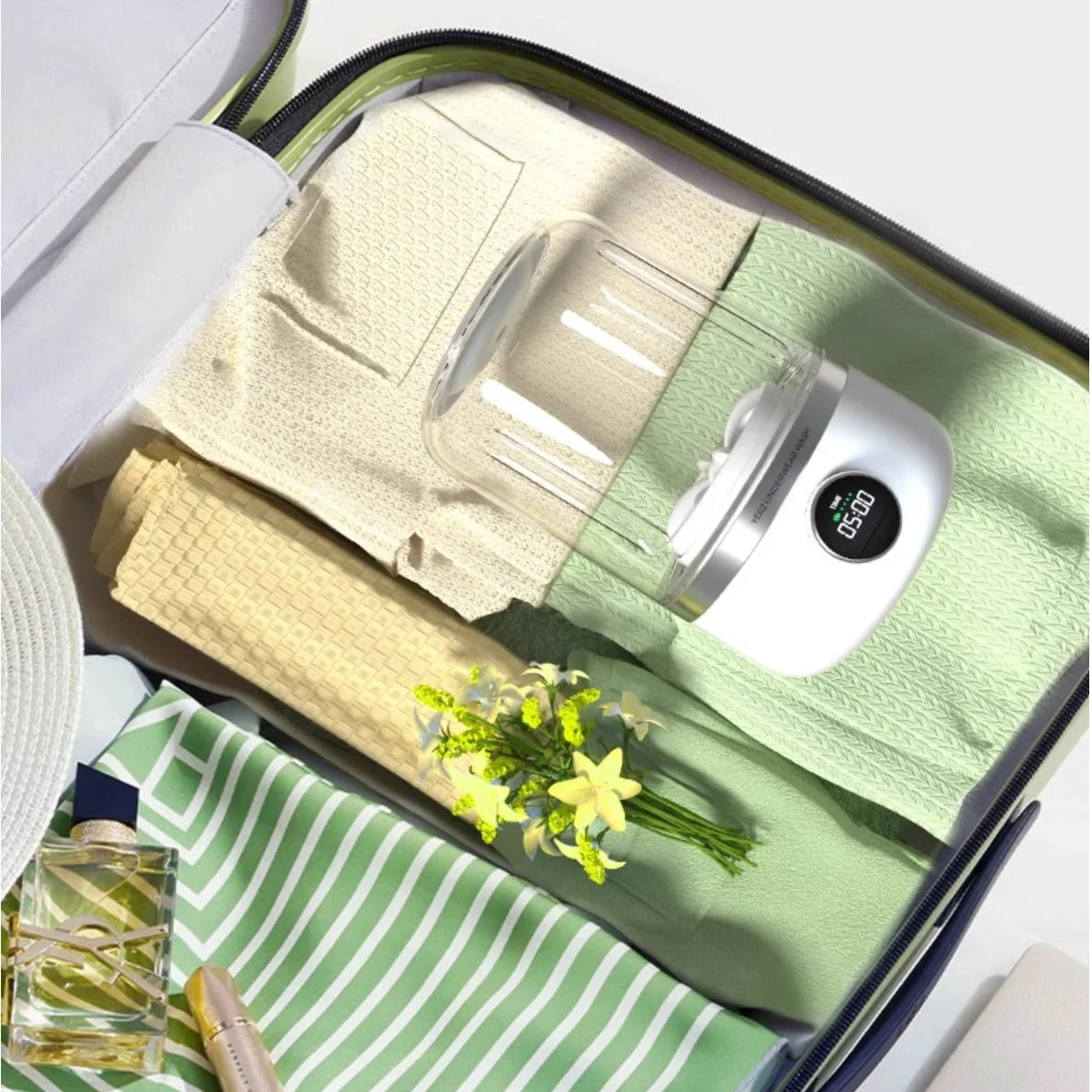 Open suitcase with folded clothes, an EDGAB mini washing machine, and a small flower on a white background